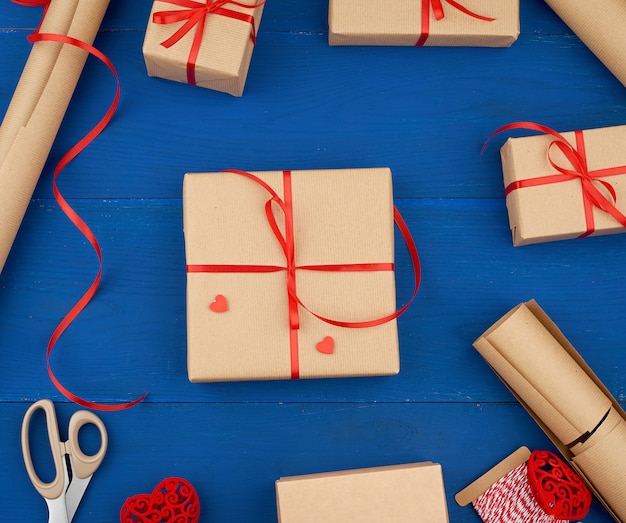 Papel kraft marrón, caja de regalo empacada y atada con una cinta roja