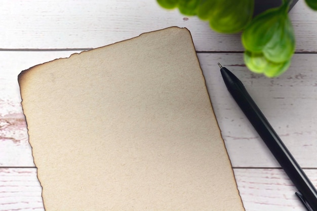 Papel marrón con borde quemado con bolígrafo en un escritorio de madera. En blanco para texto