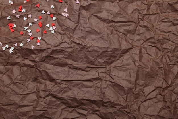 Papel marrón de textura de fondo arrugado con corazón disperso rojo rosa y blanco para el día de san valentín. foto de alta calidad