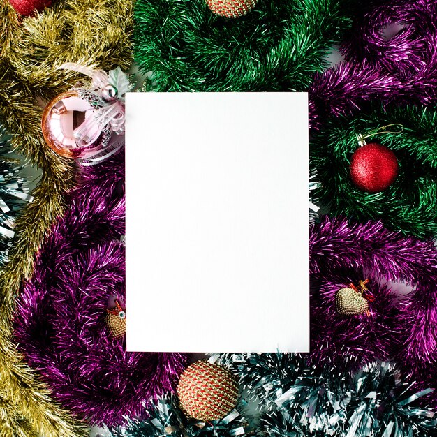Papel vacío en blanco y decoración navideña con bolas de cristal de colores, oropel, juguetes. endecha plana, vista superior