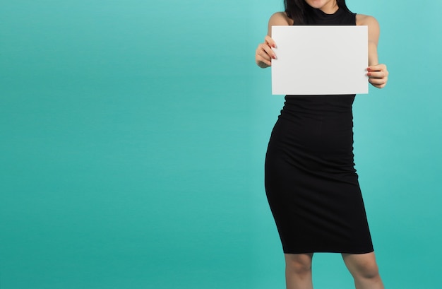 Papel vacío en blanco en la mano de la mujer sobre fondo verde o azul Tiffany. Ella usa un vestido negro.