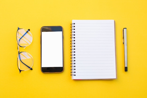Papel vazio de lápis de óculos notebook e telefone inteligente em fundo amarelo