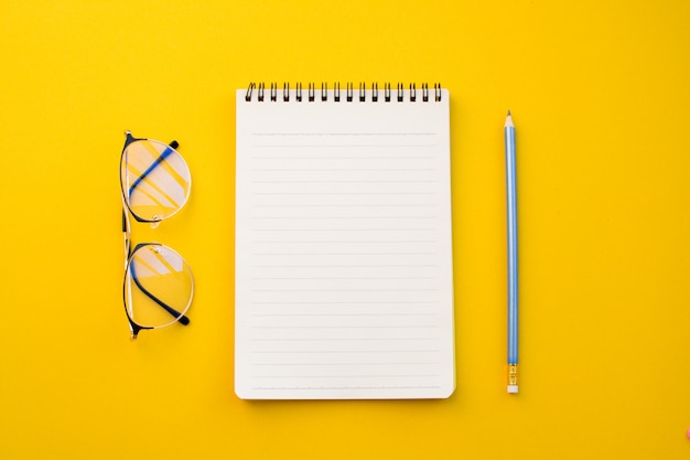 Papel vazio de óculos e lápis do caderno no fundo amarelo com conceito da escola.