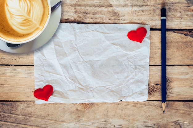 papel velho e coração vermelho, copo de café com lápis em fundo de madeira para o cartão de saudação.