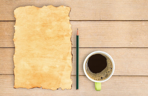 Papel viejo y lápiz con taza de café en la mesa de madera