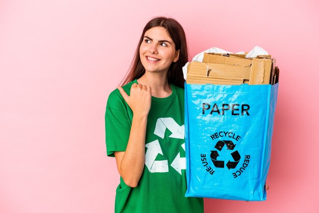 Papelão reciclado jovem mulher caucasiana, isolado em pontos de fundo rosa com o dedo polegar afastado, rindo e despreocupada.