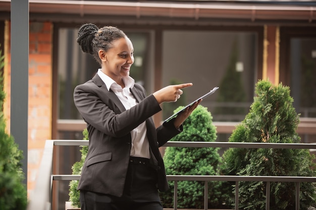 Papeleo, señalando. Empresaria afroamericana en traje de oficina sonriendo, parece confiada feliz, ocupada. Concepto de finanzas, negocios, igualdad y derechos humanos. Hermosa joven modelo, exitosa.