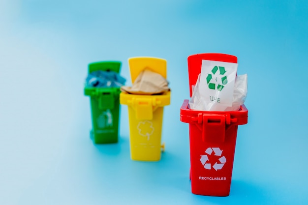 Papeleras de reciclaje amarillas, verdes y rojas con símbolo de reciclaje sobre fondo azul. Mantenga la ciudad ordenada, deja el símbolo de reciclaje. Concepto de protección de la naturaleza.