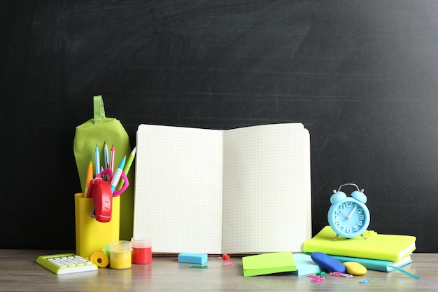 Papelería escolar diferente y cuaderno en blanco en la mesa cerca de la pizarra Espacio para texto