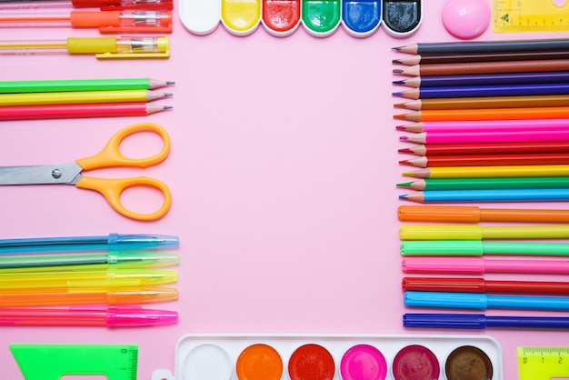 Papelería escolar lápices de pintura de colores y bolígrafos sobre fondo rosa en forma