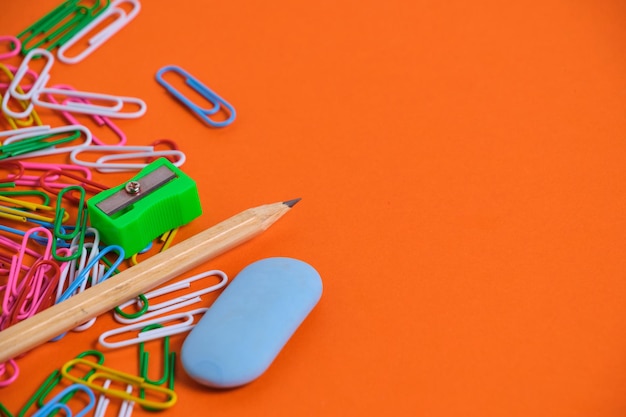 Papelería para escolares clips de papel borrador de lápiz y sacapuntas sobre un fondo naranja