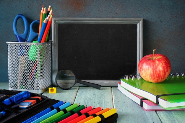 Papelería, manzana y plátano en una mesa de madera frente a la pizarra con espacio de texto