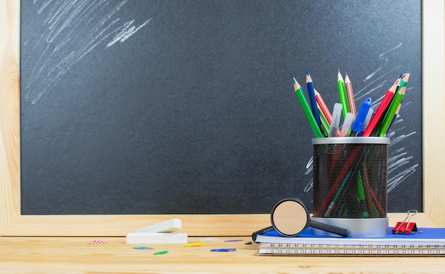 papelería en un soporte de vaso de plástico sobre una pila de cuadernos sobre una mesa de madera