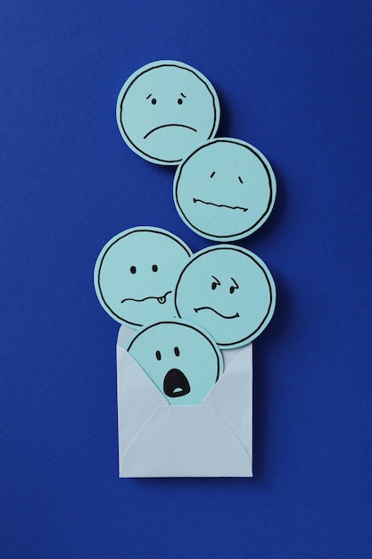 Papeles de sobre con emoji triste en la vista superior de fondo azul oscuro