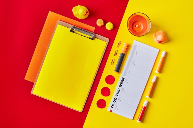 Papier auf Zwischenablage mit Planer, Kerzen, Schreibwaren in rot-gelben Farben. Flatlay-Arbeitsplatz.