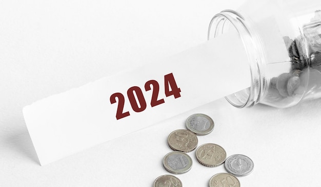 Papier mit dem Text 2024 in einem Glasgefäß auf einem Hintergrund aus Münzen