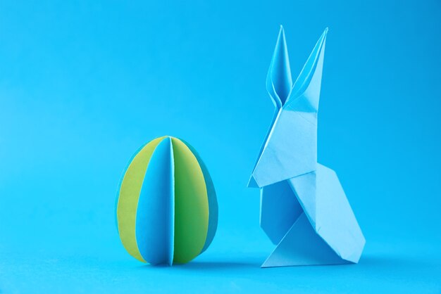 Papier Origami Esater Kaninchen und farbiges Ei an der blauen Wand. Osterfestkonzept