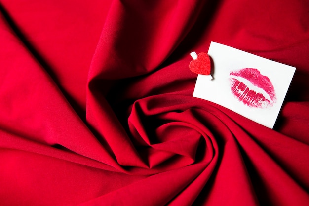 Papieraufkleber mit Kuss auf rotem zerknittertem Stoffhintergrund