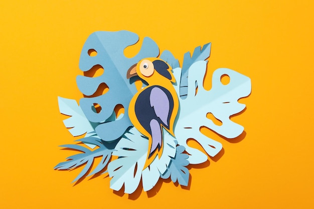 Papierblaue tropische Blätter auf gelbem Hintergrund mit einem Papagei