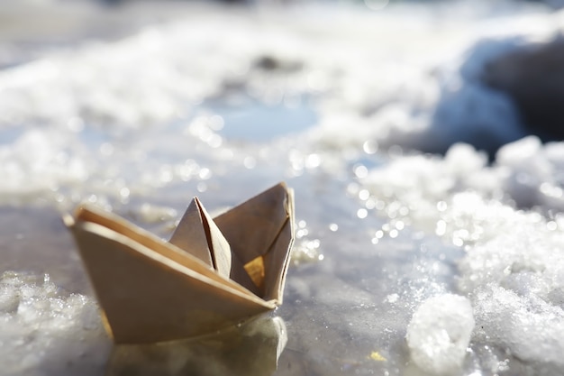 Papierboot im Wasser auf der Straße. Das Konzept des frühen Frühlings. Schmelzender Schnee und ein Origami-Boot auf Wasserwellen.