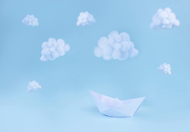 Papierboot und weiße flauschige Wolken auf hellblauer Oberfläche