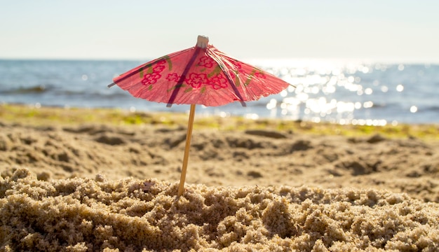 Papiercocktailschirme im Sand an der Küste an einem sonnigen hellen Sommertag