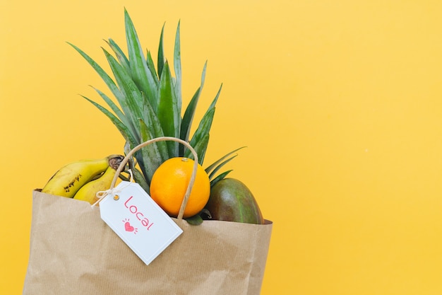 Papiereinkaufstasche gefüllt mit tropischen Früchten und Etikett mit Wort LOCAL auf gelbem Hintergrund. Platz kopieren.