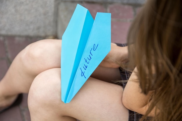 Papierflieger mit dem Wort Zukunft ist auf dem Schoß eines Teenagers Das Konzept über die Zukunft