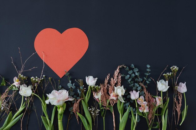 Foto papierherz auf einem dunklen hintergrund, umgeben von blumen