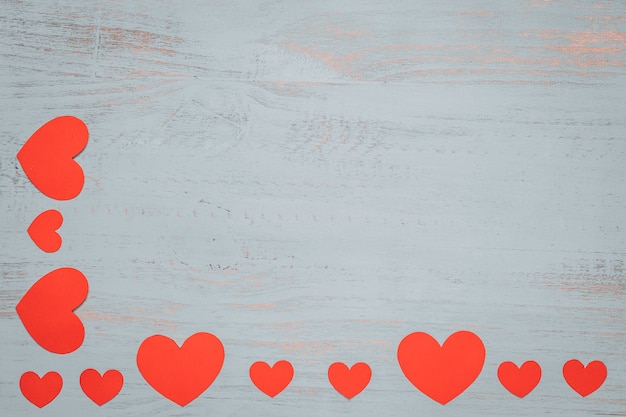Papierherzen und ein weißes Geschenk mit rotem Band auf einem hellen gemalten hölzernen Hintergrund. Seitenansicht von oben, flach gelegt. Valentinstag Konzept. Copyspace.