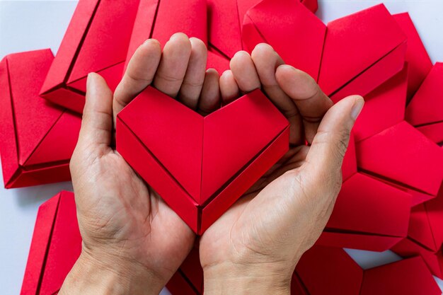 PapierherzHände, die gefaltetes Origami-Herz weißen Hintergrund haltenKleine Jungen halten rotes Herz in der Hand