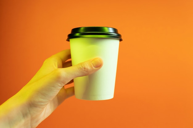 Papierkaffeetasse in einer Hand in einem modischen Neonlicht.