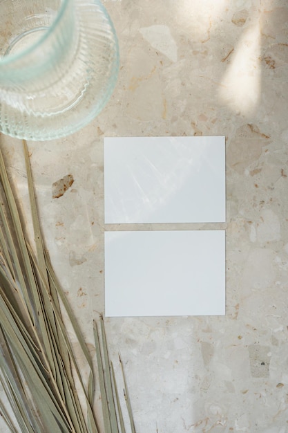 Papierkarte mit leerem Mockup-Kopierraum und getrocknetem Palmblatt auf Marmor-Tisch-Hintergrund mit Schattensilhouette im sanften Sonnenlicht