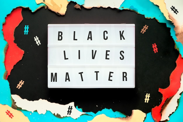 Papierloch mit verbrannten Kanten, Text Black Lives Matter auf Leuchtkasten, umgeben von Hashtags