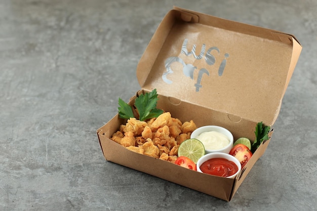 Papierschachtel mit lecker gebratenem Popcorn-Huhn auf grauem Hintergrund