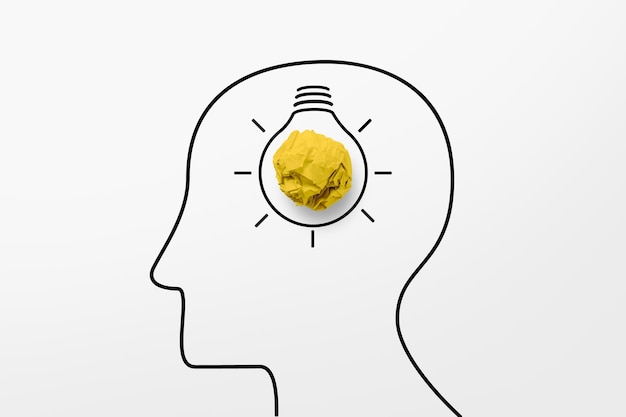 Papierschrottball gelbe Farbe und Glühbirne im menschlichen Kopfsymbol. Kreatives Ideenkonzept.