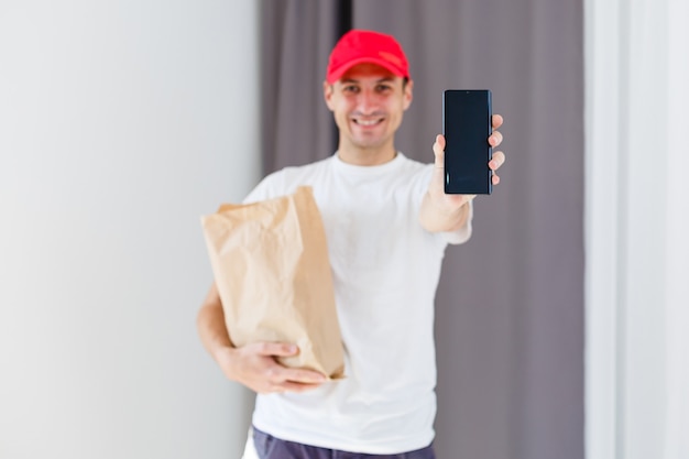 Papiertasche und Lebensmittelbehälter in den Händen eines lächelnden Lieferboten. Qualitätsservice eines Restaurants.