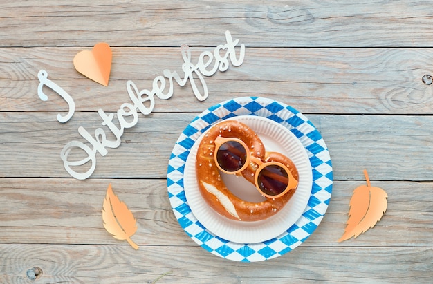 Papiertext "Ich liebe Oktoberfest", flach auf rustikalem Holztisch mit lustiger Brezel liegend