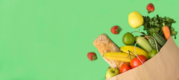 Papiertüte mit Gemüse, Obst und Baguette auf grünem Hintergrund, Draufsicht, Kopierraum