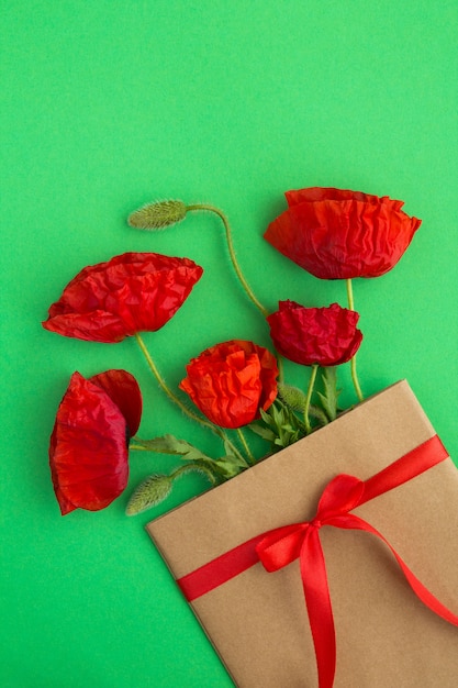 Papoilas vermelhas em um envelope amarrado com uma fita vermelha na superfície verde. Primavera ou verão conceito de flores.