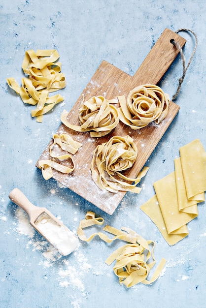 Pappardelle, fettuccine ou tagliatelle italianos amarelos crus da massa, fim acima. ovo macarrão caseiro processo de cozimento, macarrão longo enrolado, espaguete cru.