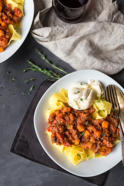 Pappardelle-Nudeln mit Fleischragout mit Kürbis- und Burrata-Käse auf grauem Betonhintergrund. Italienische Küche. Draufsicht.