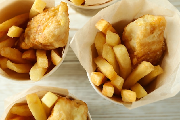 Pappbecher mit gebratenem Fisch und Chips auf hölzernem Hintergrund