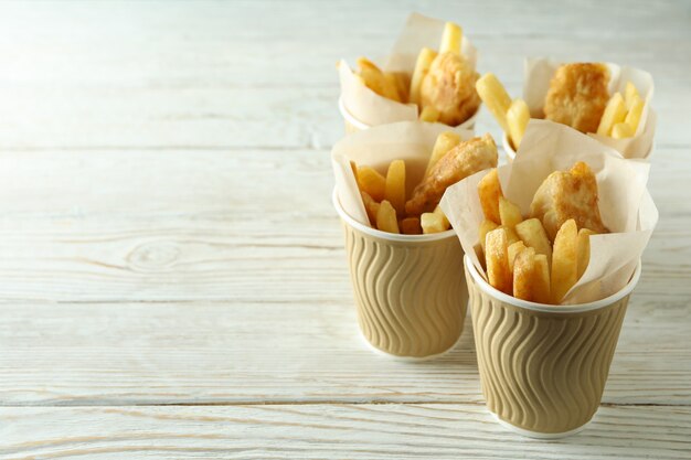 Pappbecher mit gebratenem Fisch und Chips auf hölzernem Hintergrund