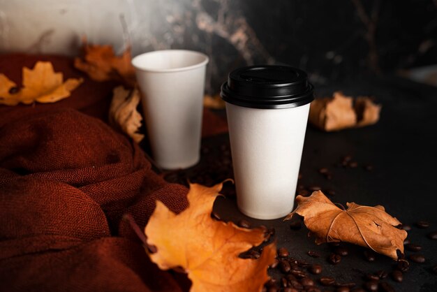 Pappbecher mit Kaffee auf dunklem Hintergrund. Herbst, Kaffeezusammensetzung. Kaffee zum Mitnehmen. Ahornblätter, brauner Schal. Flach liegen. . Foto in hoher Qualität