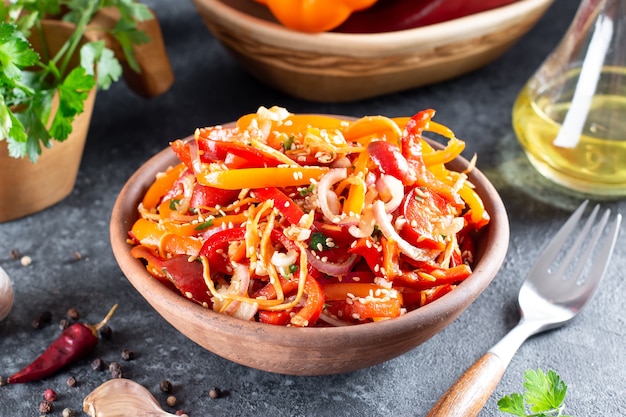 Paprika mit koreanischen Karotten, Sesam und Gemüse in einer Schüssel auf dunklem Hintergrund. Scharfes gesundes Essen