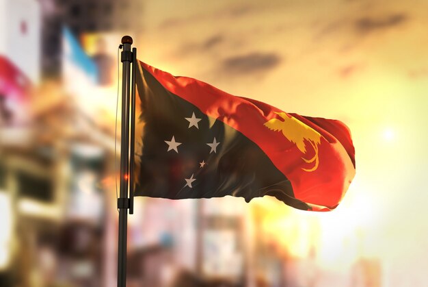 Papua-Neuguinea-Flagge gegen Stadt verschwommener Hintergrund bei Sonnenaufgang-Hintergrundbeleuchtung