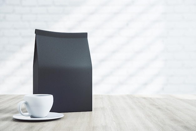 Paquete de café negro en blanco con un copyspace y una taza blanca en la mesa de madera Mockup