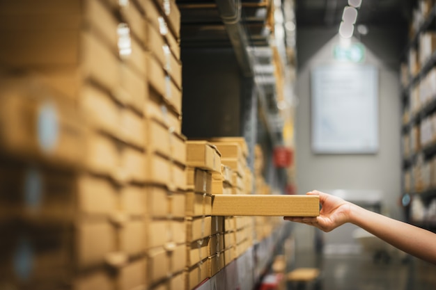 Paquete de caja de cartón con desenfoque de mano de mujer comprador recogiendo producto del estante en el almacén.