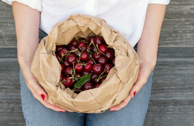 Paquete ecológico lleno de cerezas rojas maduras en manos de mujeres en jeans.